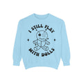 A light blue crewneck sweatshirt featuring a black graphic of a stitched voodoo doll with the text 'I STILL PLAY WITH DOLLS' arched above and below it, displayed on a clean white background.