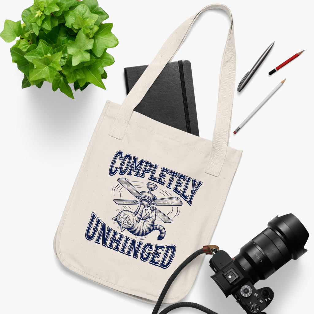 Tote bag with 'Completely Unhinged' design on a white surface with stationery items.