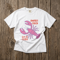 White t-shirt with pink lobster graphic and text on a wooden surface