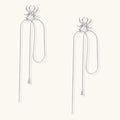 White gold plated spider earrings with pearl body and long threader chains on beige background