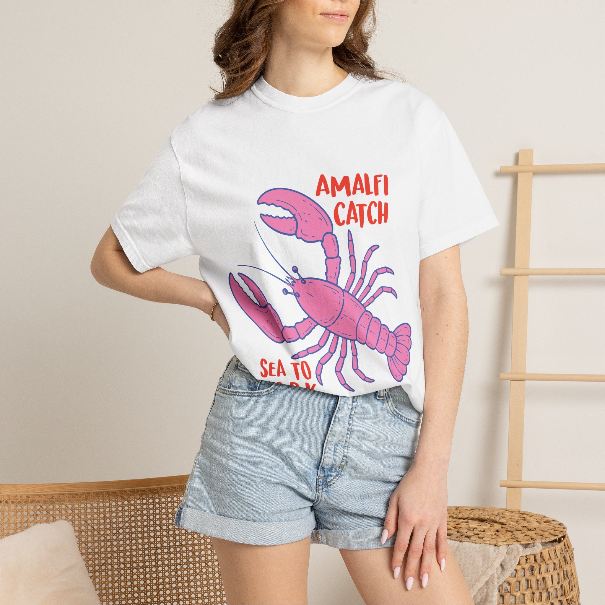 Person wearing a white t-shirt with a pink lobster graphic and text, standing against a neutral background.
